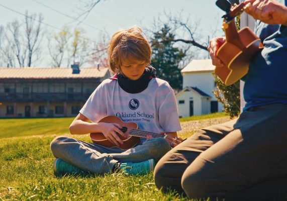 Photo of a kid from the Oakland School learning to play the ukulele
