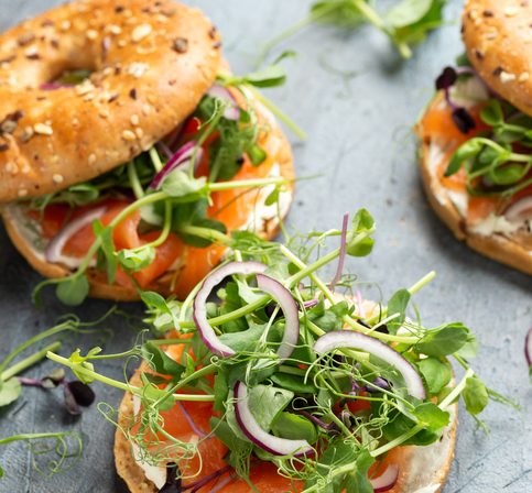 Smoked salmon and soft cheese seeded bagel with pea and purple reddish shoot salad and red onion.