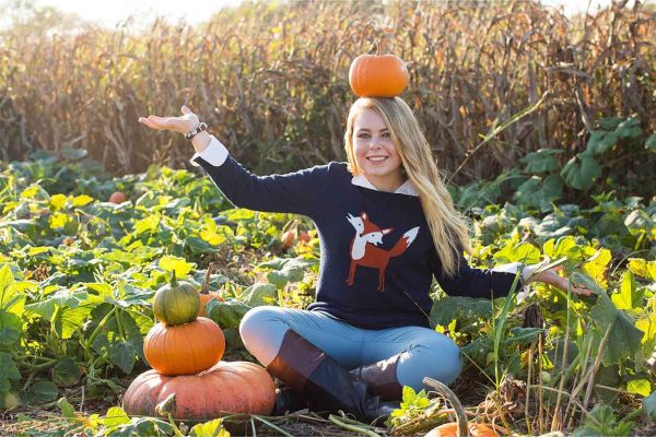 A girl sitting in a pumpkin patch and balancing a pumpkin on her head