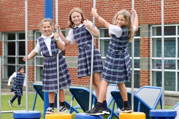 girls in plaid uniforms play on playground smiling