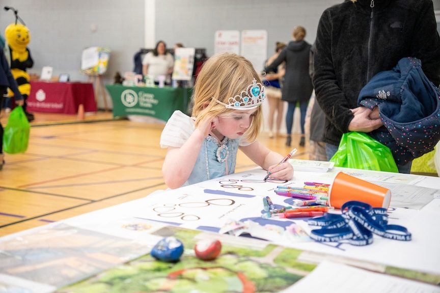 Little girl in a blue princess dress an tiara draws at the CharlottesvilleFamily Camp Expo and KidFest